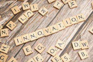 Scrabble tiles on a wooden table spell 'INNOVATION' with scattered letters around the board.