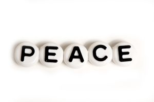 Five white round beads spell the word 'PEACE' in black letters on a white background, arranged in a row.