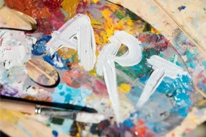 Colorful artist's palette with dried paints and a bold white word ART painted across it, with a brush nearby.