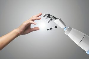 Human hand reaching toward a white robotic hand, fingers nearly touching in a soft-lit scene.