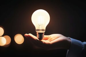 Hand holding a glowing light bulb in a dark background, symbolizing ideas and innovation.