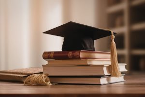 Graduation cap resting on a stack of books on a wooden table, symbolizing academic achievement.