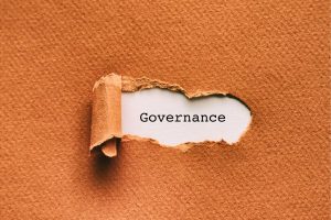 Ripped paper reveals the word 'Governance' on an orange textured background, emphasizing governance concepts.
