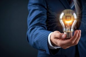 Businessperson in a blue suit holding a glowing light bulb with circuit lines, symbolizing innovation and technology.