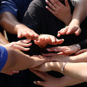 Close-up of several hands stacked on top of one another, showing rings and bracelets, symbolizing teamwork and unity.
