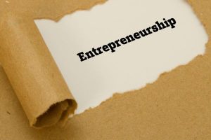 Torn piece of white paper with the word 'Entrepreneurship' on a brown paper background, suggesting a concept draft or idea theme.