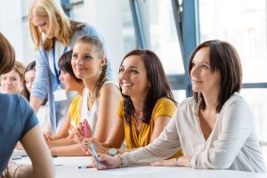 Group of women seated at a bright table in a workshop, smiling and taking notes.”