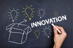 Hand sketching chalk drawings of light bulbs around a box on a dark chalkboard, with the word INNOVATION written prominently.