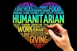Colorful heart-shaped word cloud about humanitarian giving, with a hand holding a pen drawing on the right against a black background.