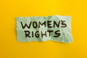 Torn mint-green paper with the handwritten text 'WOMEN'S RIGHTS' on a bright yellow background, symbolizing advocacy.