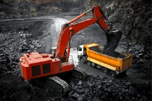 Orange excavator loading crushed rock into a yellow dump truck at a quarry site.