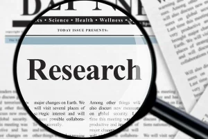 Magnifying glass over a newspaper, highlighting the word 'Research'.