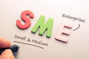 Colorful wooden letters spell SME with 'Small & Medium Enterprises' underlined by a hand drawing a line with a marker.