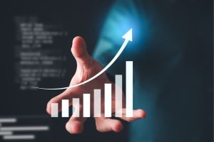 Hand extending under a rising bar chart and upward arrow, illustrating business growth.