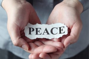 Hands cupped together holding a torn paper strip with the word PEACE.