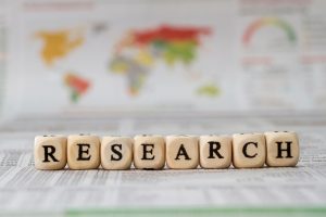 Row of wooden blocks spelling RESEARCH on a newspaper with a blurred world map in the background.