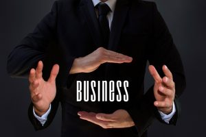 Businessman in a dark suit forms a protective frame around the word BUSINESS with his hands.