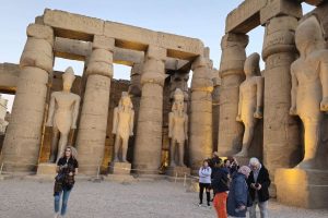 Ancient Egyptian temple ruins with tall stone statues and massive columns, as tourists explore.